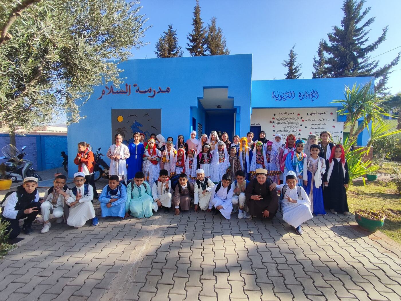 تلميذات وتلاميذ بأزياء مغربية تقليدية أمام جدار المدرسة الأزرق